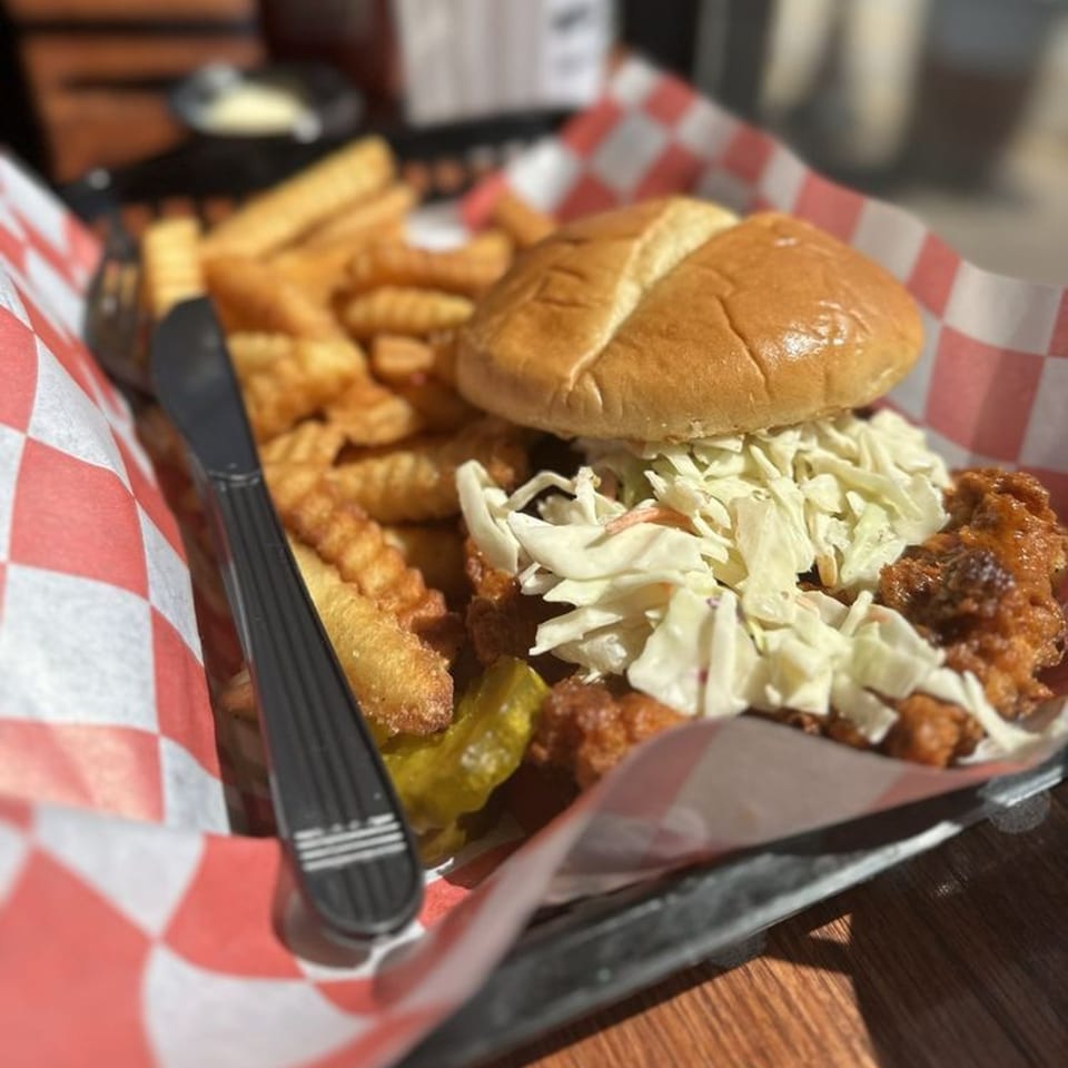 My Brothers Place Parkville's fried chicken sandwich with coleslaw, pickles, and waffle fries in a basket.