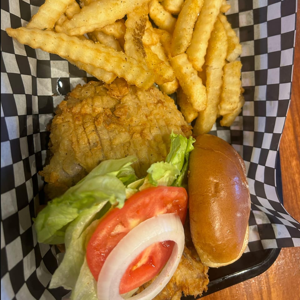 My Brothers Place fried fish sandwich with lettuce, tomato, onion, and a side of crinkle-cut fries.