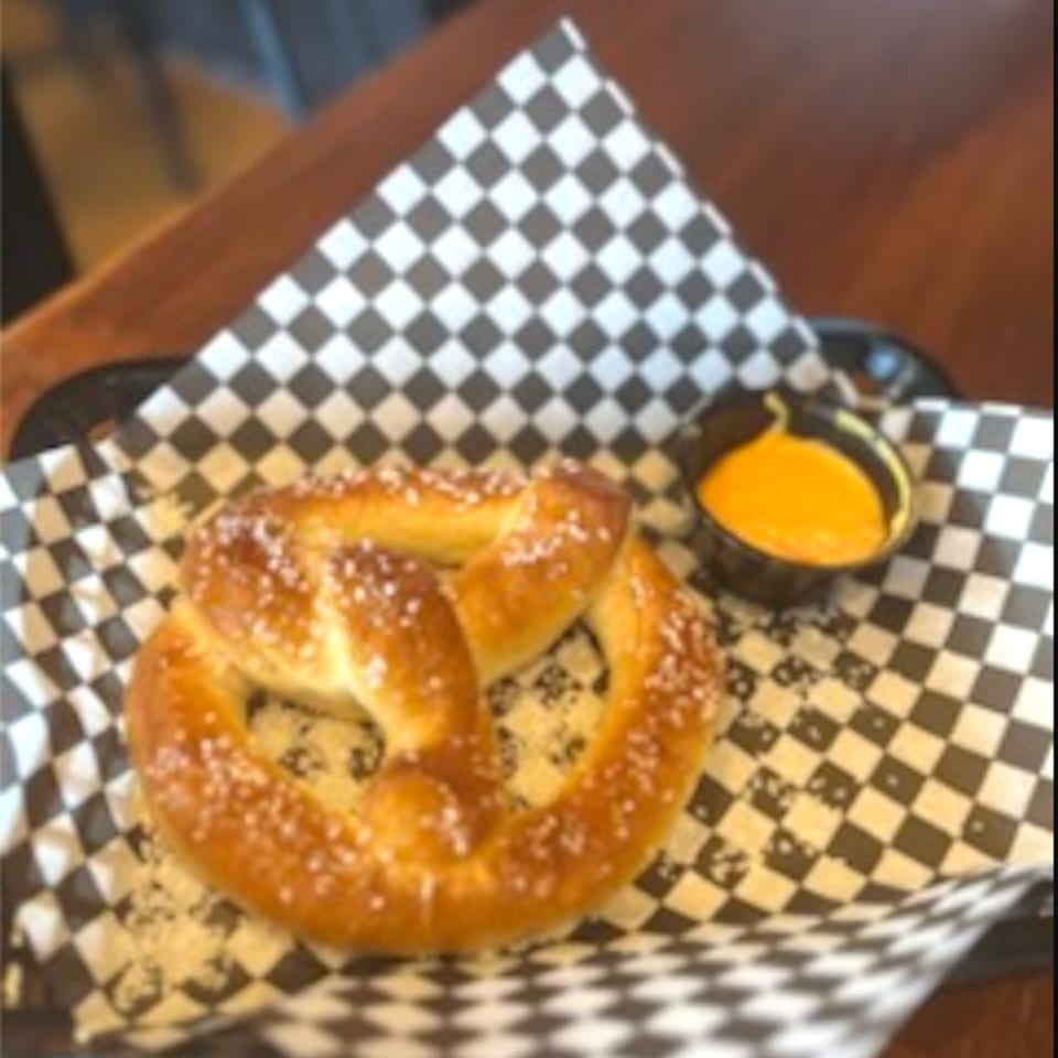 A salted pretzel with a side of cheese dip on checkered paper from My Brothers Place.