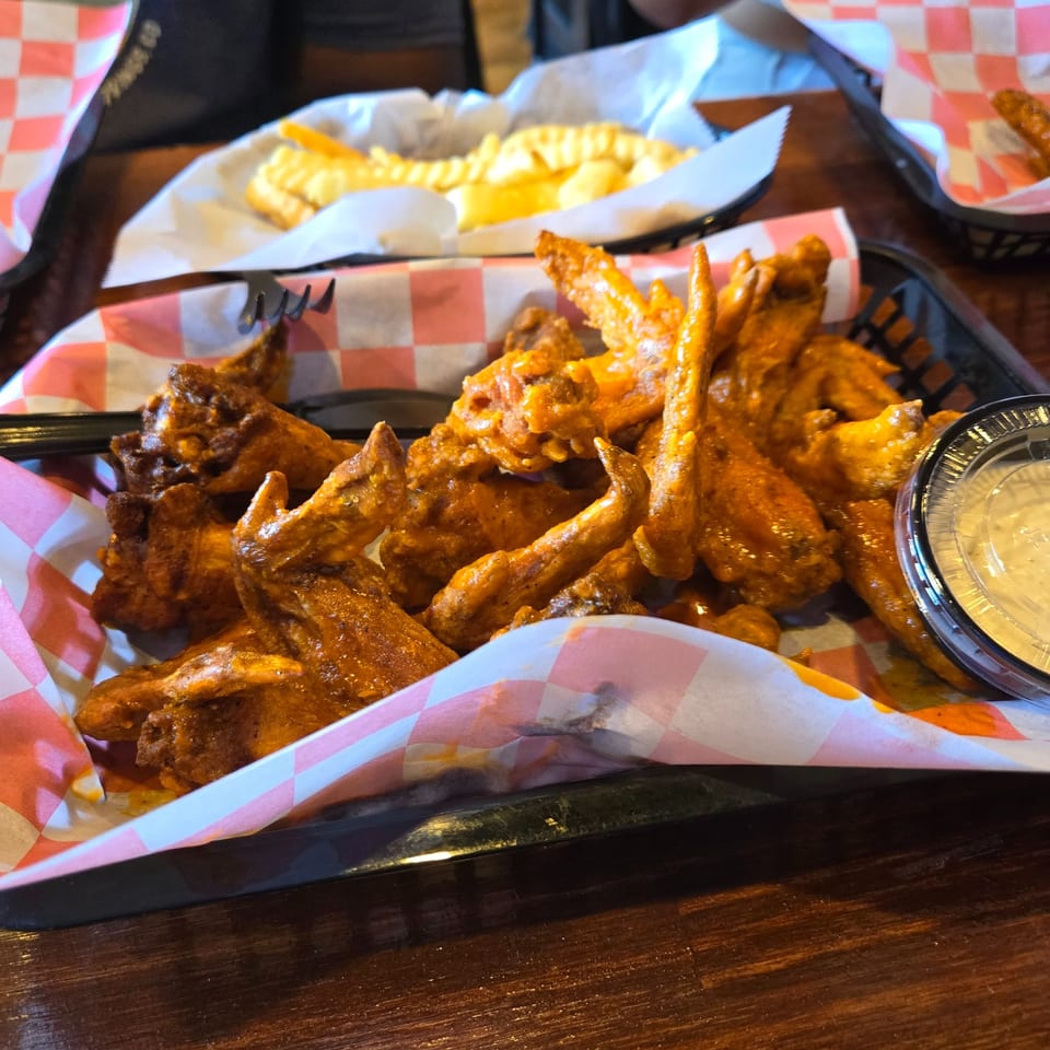 A basket of buffalo wings with a side of ranch dressing and a basket of waffle fries.